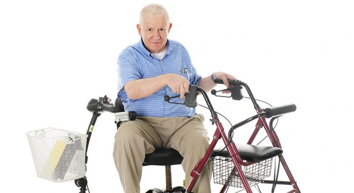 A senior man sitting sideways on his power scooter while holding onto the handles of his wheeling walker. On a white background.