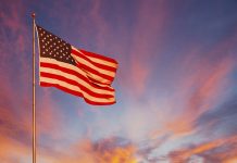 An orange and pink sunset surround the American Flag and makes it glow with pride.