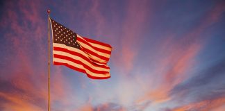 An orange and pink sunset surround the American Flag and makes it glow with pride.