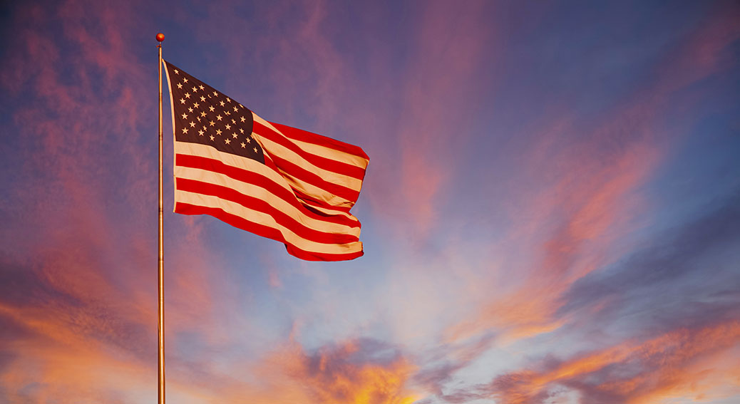 An orange and pink sunset surround the American Flag and makes it glow with pride.