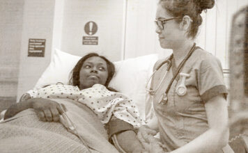 Medicaid patient laying in bed with nurse at her bedside
